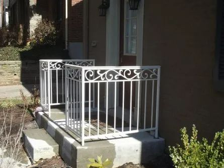 White wrought iron railings on a concrete porch steps leading to a home with brown siding and a window.