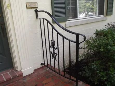 Black iron handrail beside a brick step and beige building.