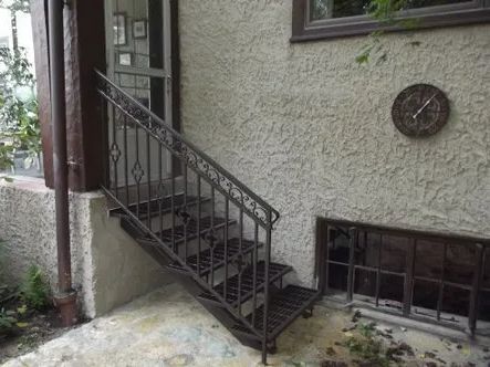 Exterior metal staircase leading up to a doorway. Brown railings and stairs against a textured wall.