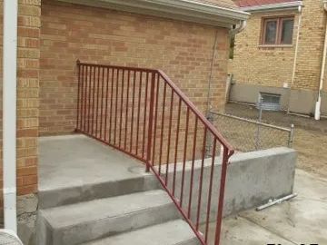 Red metal railing on concrete steps against a brick wall.