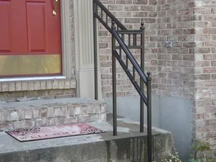Brown metal handrail on brick steps leading to a red door.