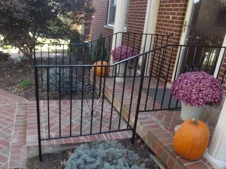 Black metal railing on a brick porch, with pumpkins and potted mums; front of a house.