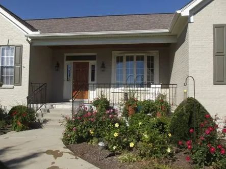 House exterior with porch, steps, and landscaping. Beige brick, brown door, and colorful flowers.