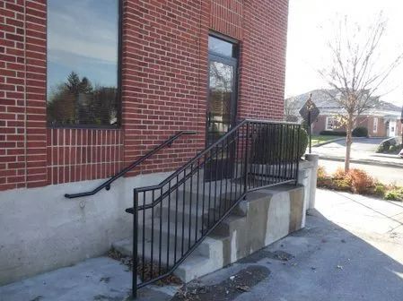 Brick building exterior with concrete steps and black metal railings leading to a doorway.