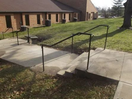 Exterior stairs with black handrails and a concrete landing leading to a building.