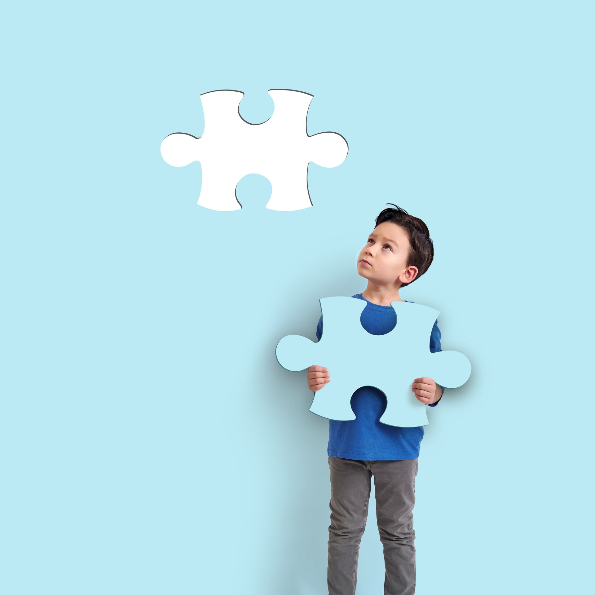 Little boy holding a blue piece of puzzle that fits into the background