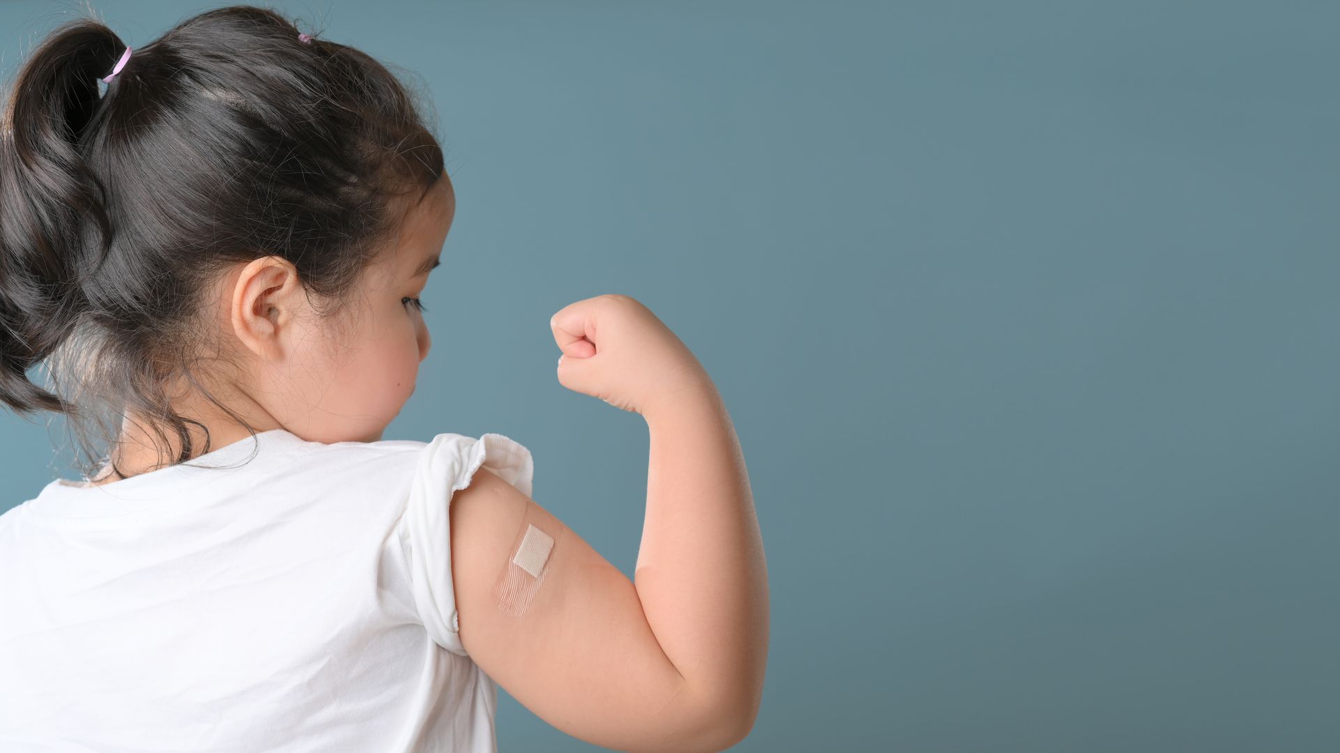 Little girl flexing her arm to show a band-aid over an injection site