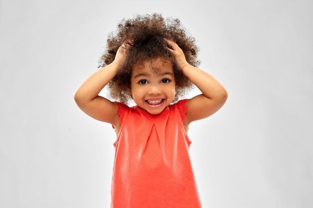 A little girl in a red dress is holding her hair in her hands.