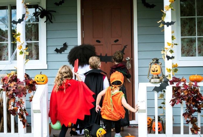 A group of children in halloween costumes are standing on a porch.