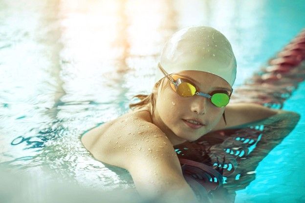 A young girl wearing a swim cap and goggles is swimming in a swimming pool.