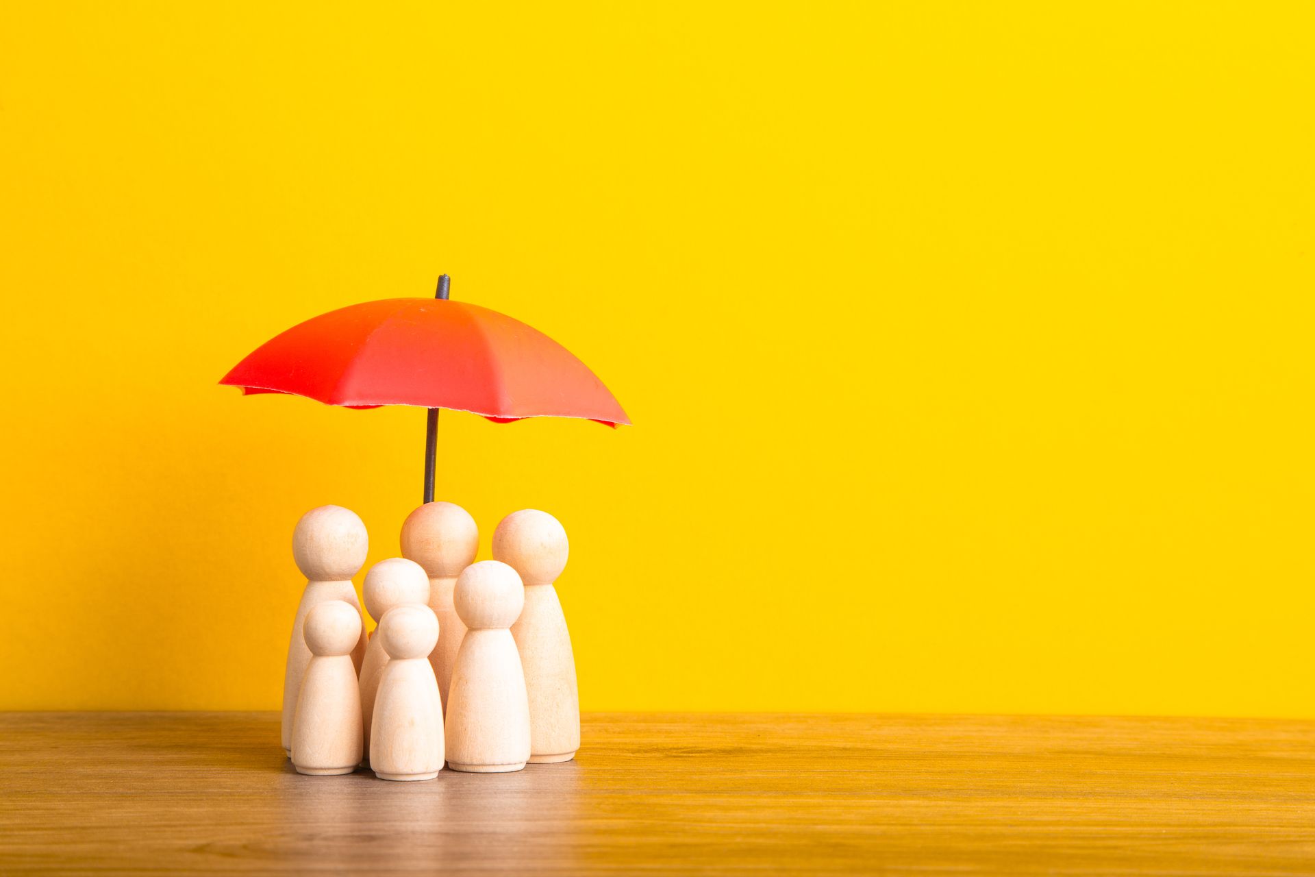 Family of wooden pins under a red umbrella against a yellow background
