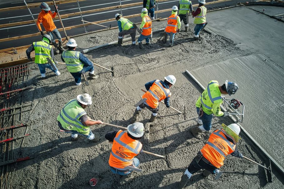 Construction workers in orange and neon vests paving a road with gravel and asphalt machines