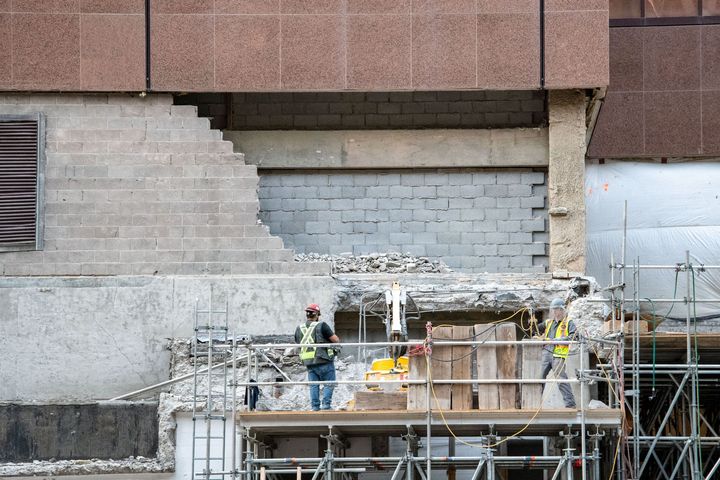 Construction workers on scaffolding repairing a building wall with concrete and metal framing