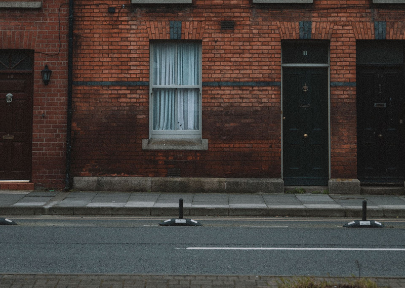 Red brick building façade with a window, black door, and curbside street in front.