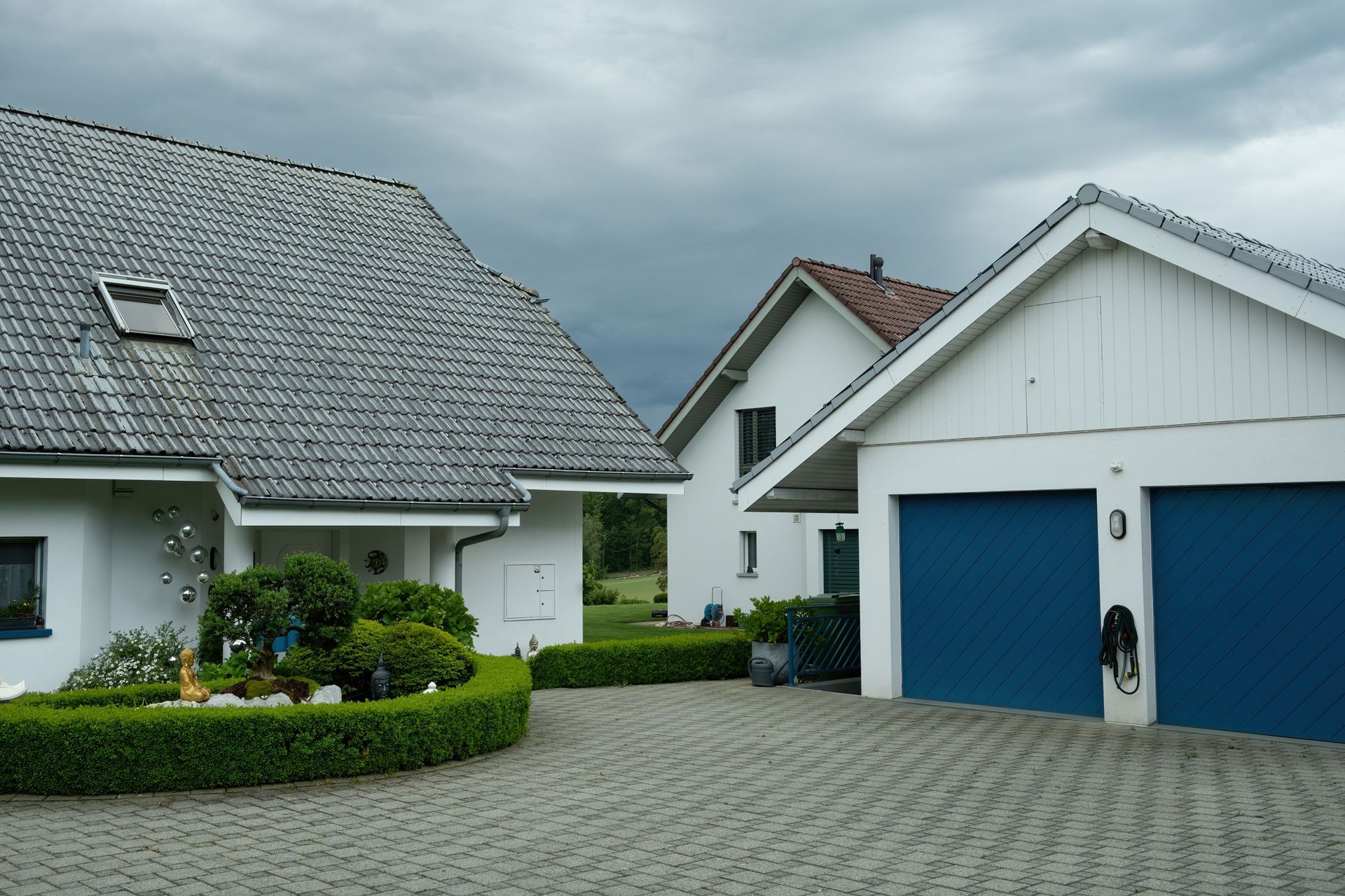 Modern suburban houses with gray roofs, blue garage doors, and a paved driveway under an overcast sky