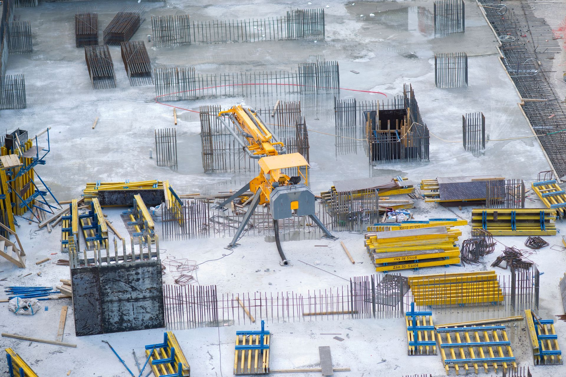 Construction site with concrete foundations, rebar, and yellow excavators in winter snow