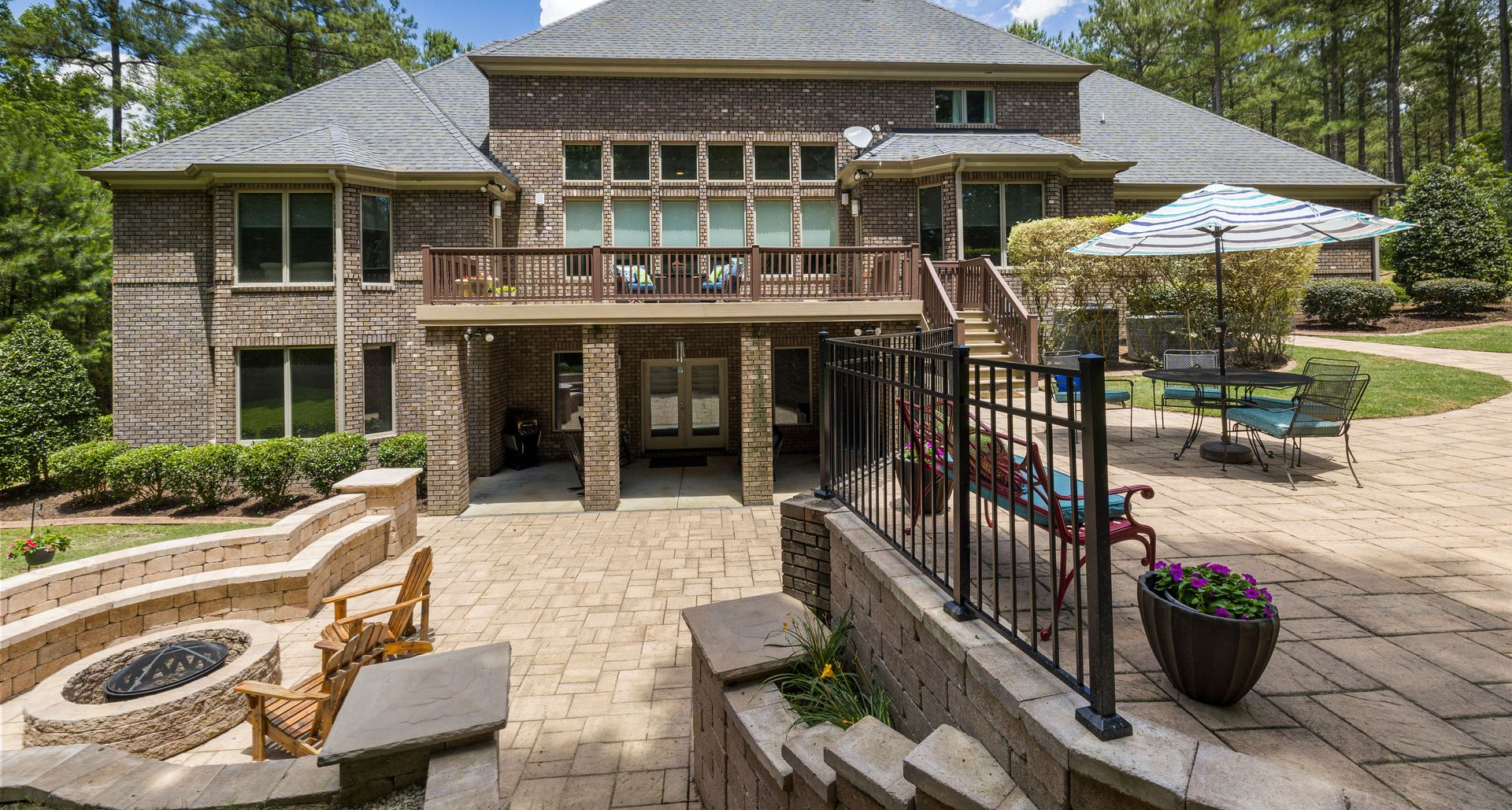 Stone house with a patio, outdoor fireplace, stairs, and a deck with umbrellas and potted plants