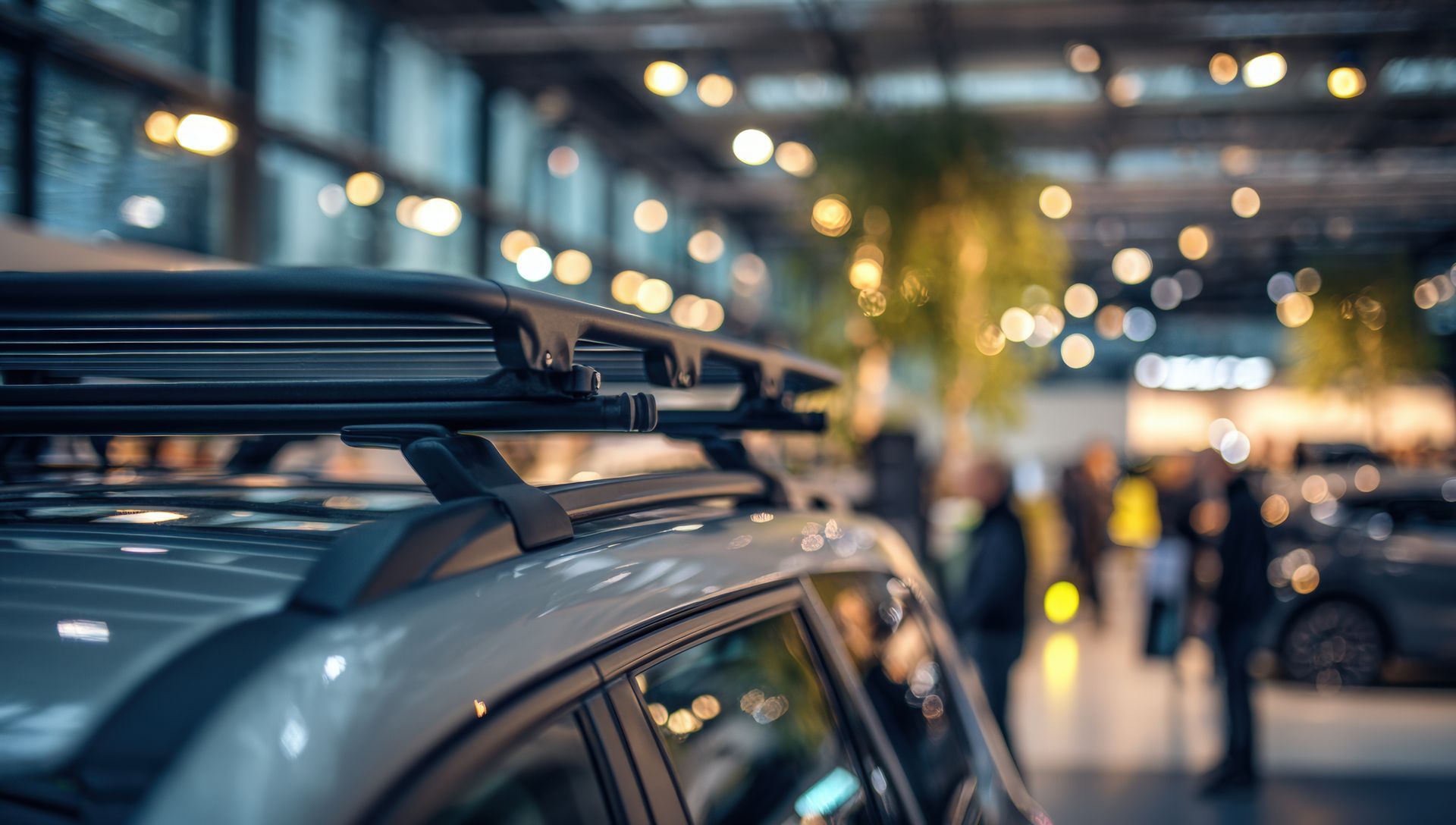 Close-up of a car with roof rack parked on a city street at dusk, with blurred headlights and pedestrians in background