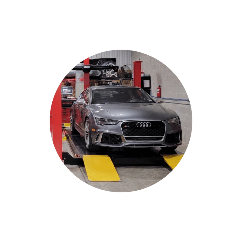 Audi vehicle positioned on a wheel alignment rack inside an automotive repair shop during a precision alignment service.