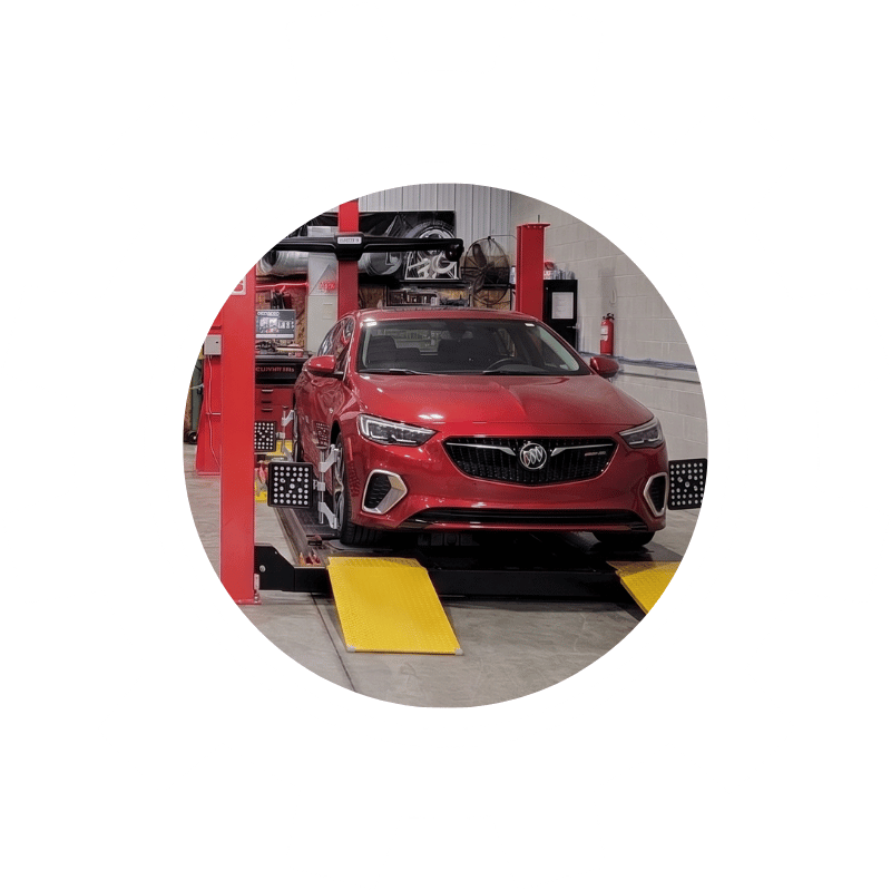 Red Buick sedan secured on a wheel alignment machine inside a professional automotive service facility.