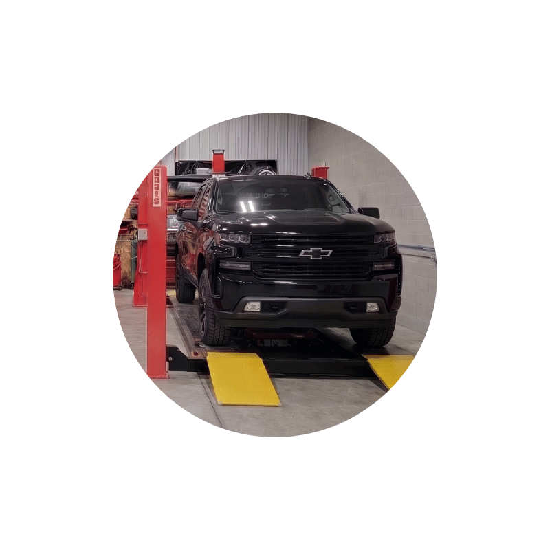 Black Chevrolet pickup truck on a wheel alignment rack during suspension and steering system adjustment.