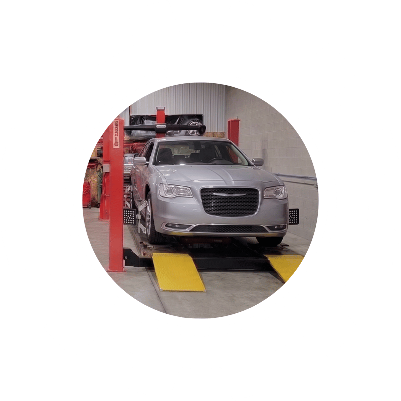 Silver Chrysler sedan positioned on alignment equipment inside an automotive repair and maintenance shop.