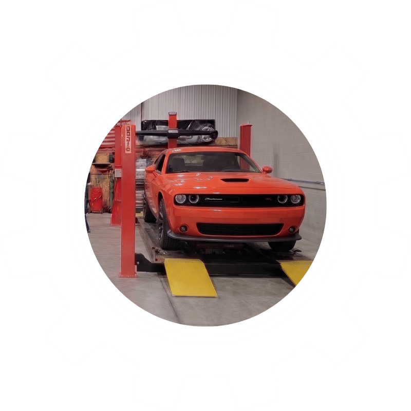 Orange Dodge Challenger muscle car on a wheel alignment rack during handling and tire wear correction service.