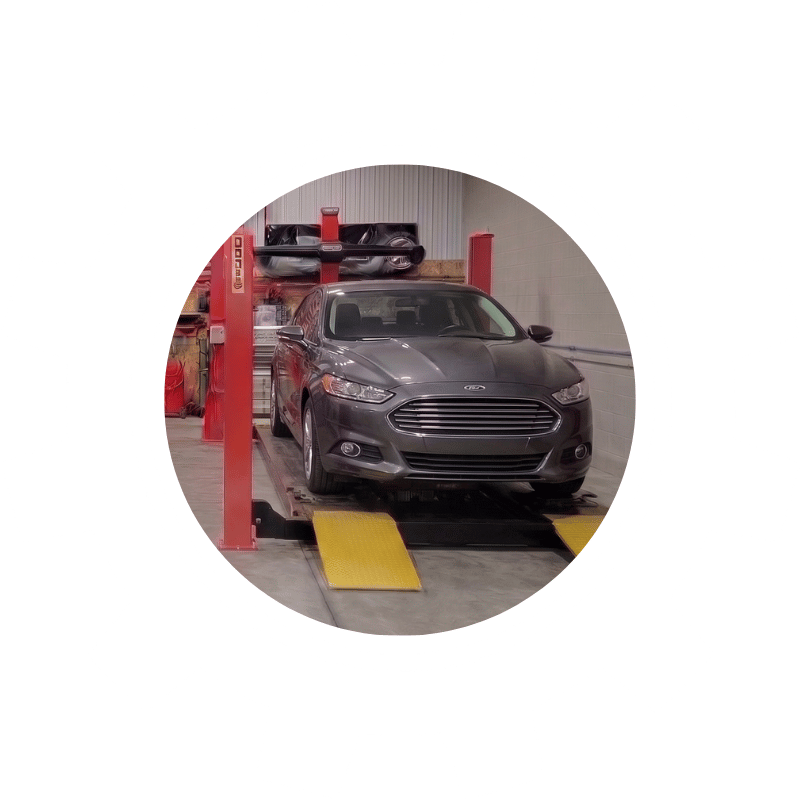 Gray Ford sedan secured on professional wheel alignment equipment inside a vehicle repair facility.