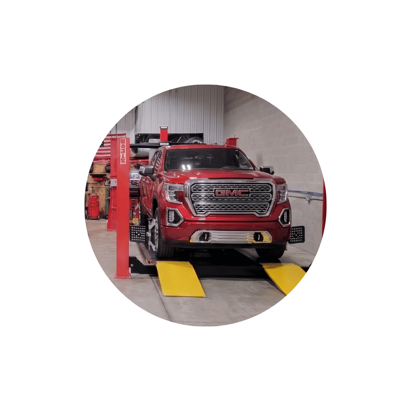 Red GMC pickup truck undergoing wheel alignment service to improve steering accuracy and tire performance.