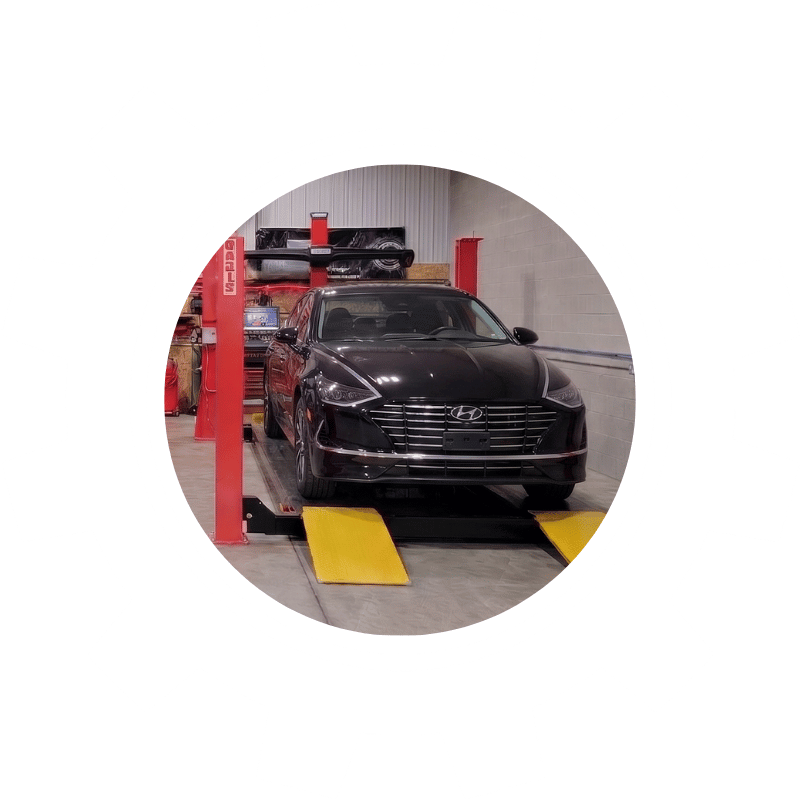 Black Hyundai sedan positioned on an alignment rack during suspension and steering system inspection.