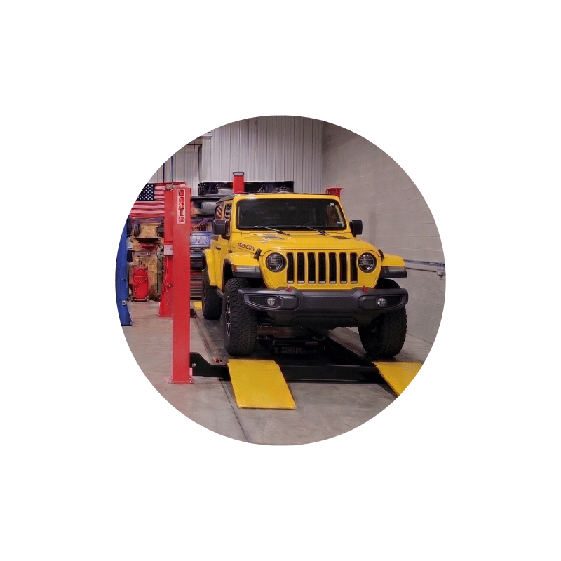 Yellow Jeep Wrangler on a wheel alignment machine inside an automotive repair shop.