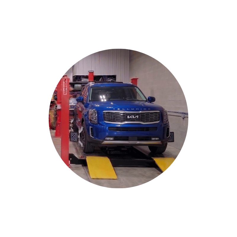 Blue Kia SUV secured on a wheel alignment rack for tire wear prevention and handling optimization.