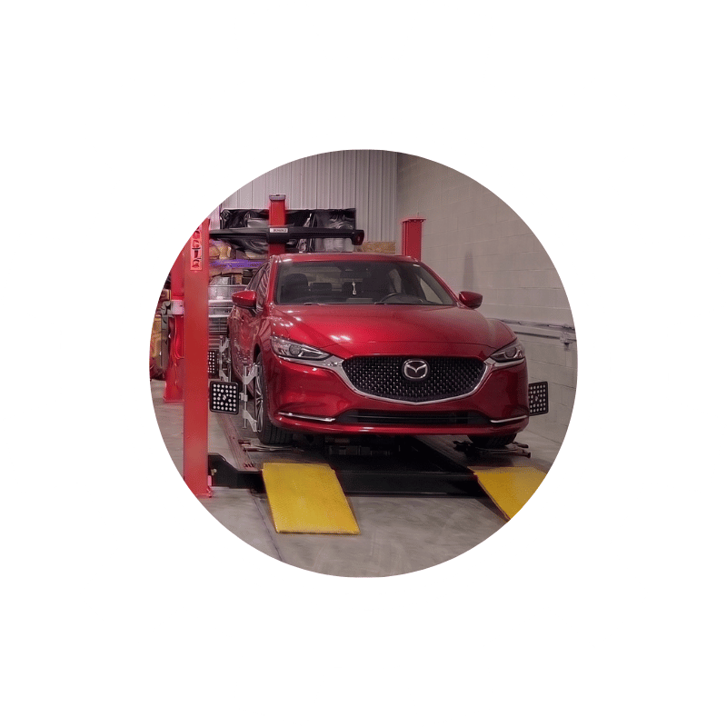 Red Mazda sedan secured on an alignment rack during precision steering and suspension adjustment.
