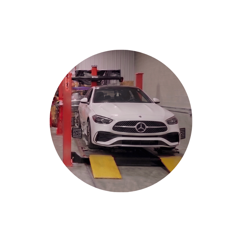White Mercedes-Benz sedan positioned on wheel alignment equipment inside an automotive repair shop.