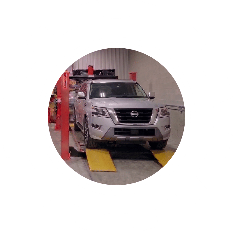 White Nissan SUV on a wheel alignment rack during suspension inspection and alignment correction.