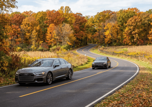 Audi and Mercedes-Benz sedans driving along a winding New Lenox road surrounded by colorful fall foliage