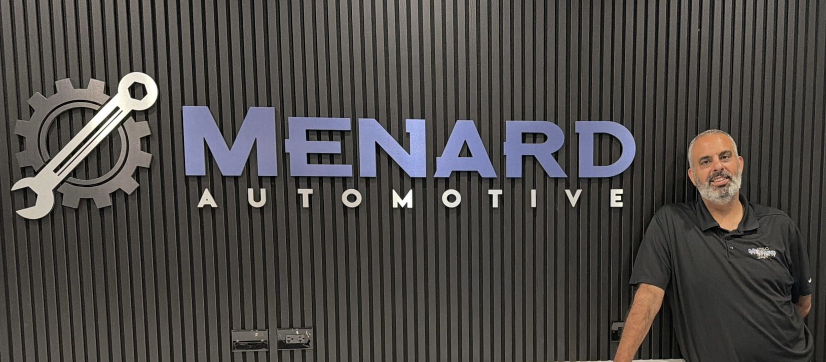 Menard Automotive sign on a dark wall with Sam, the owner, standing at the right