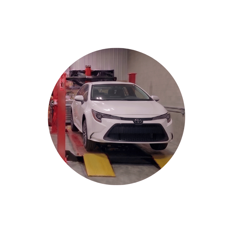 White Toyota sedan positioned on a wheel alignment machine inside a vehicle service center.