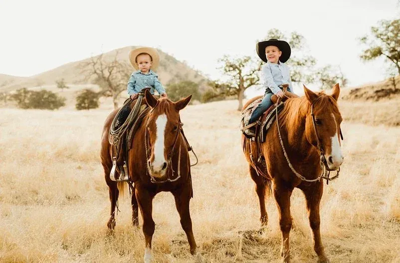 Two young boys are riding horses in a field.