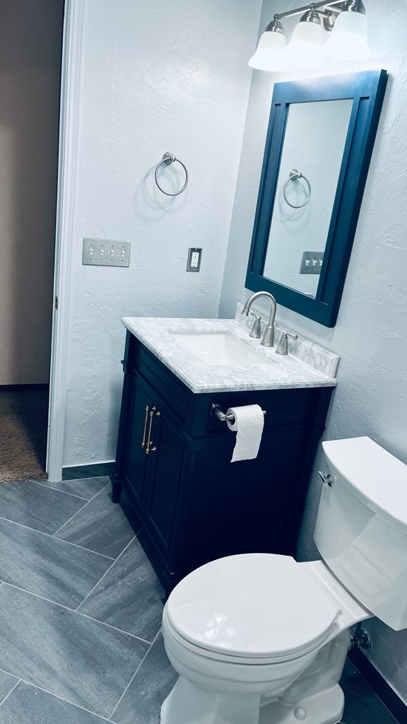 Dark blue vanity with white countertop, toilet, and mirror in a bathroom with gray-tiled floor.