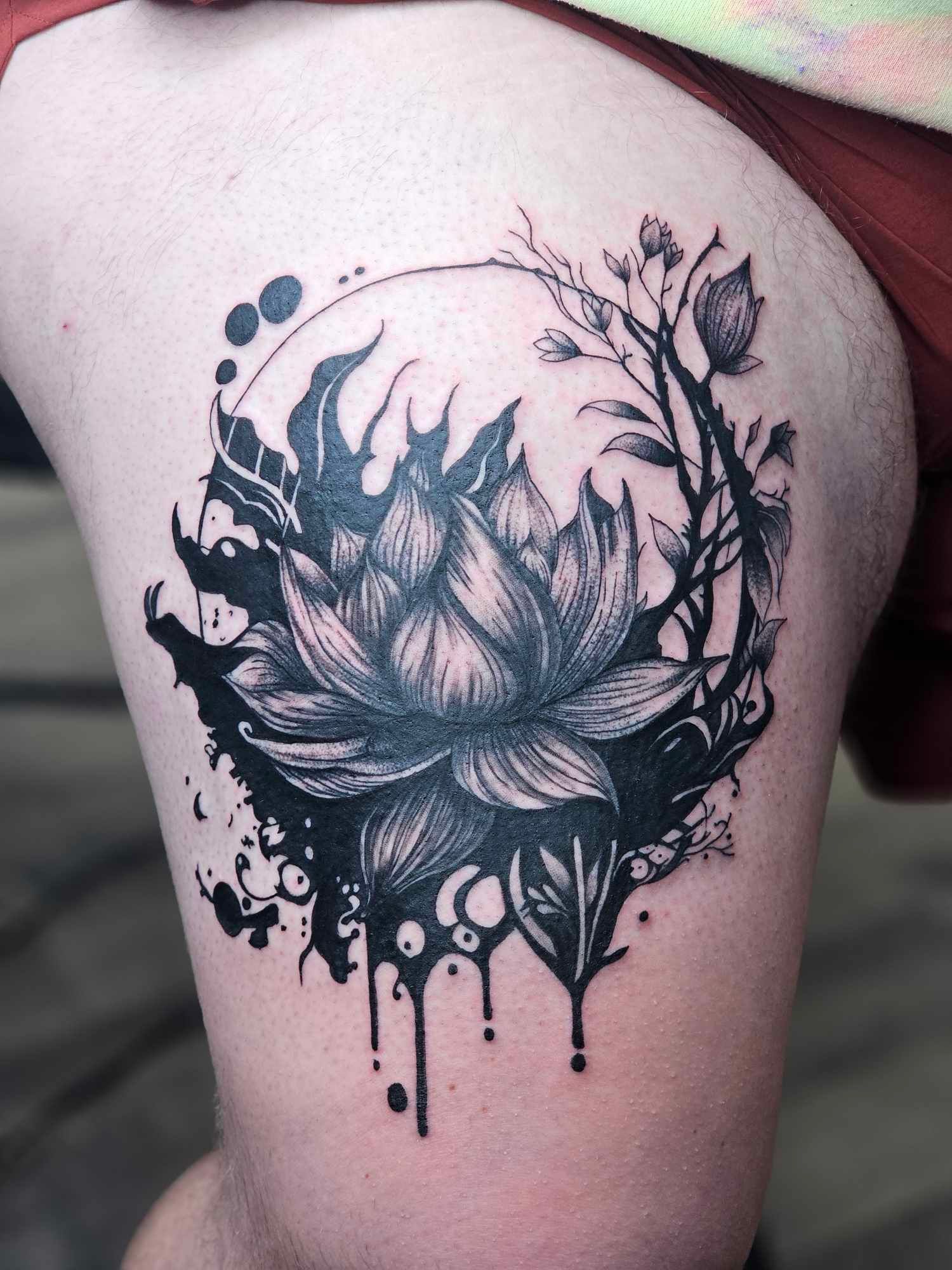 A black and white tattoo of a lotus flower on a person 's thigh.