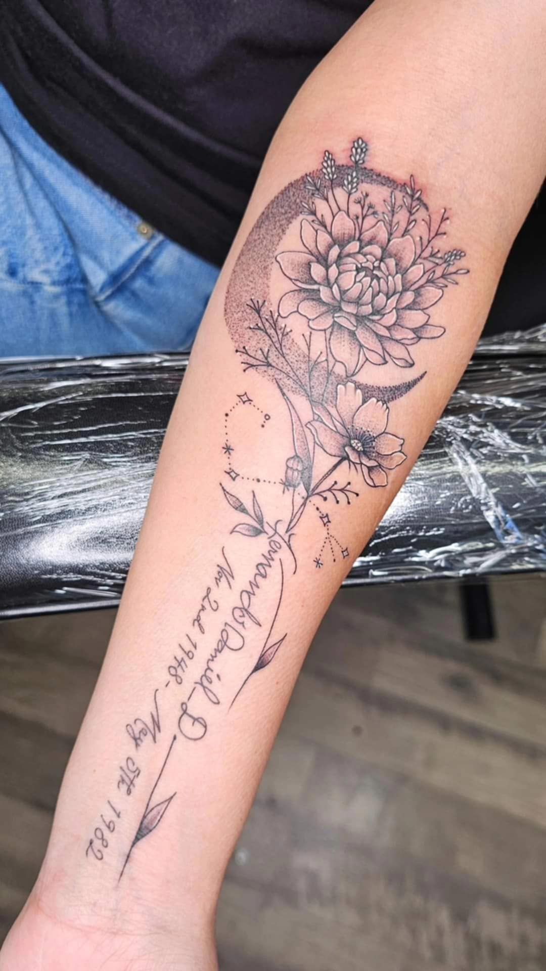 A woman has a tattoo of a flower and a crescent moon on her forearm