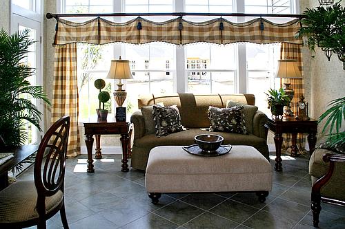 Living room with sofa, ottoman, and checkered curtains; plants and lamps.