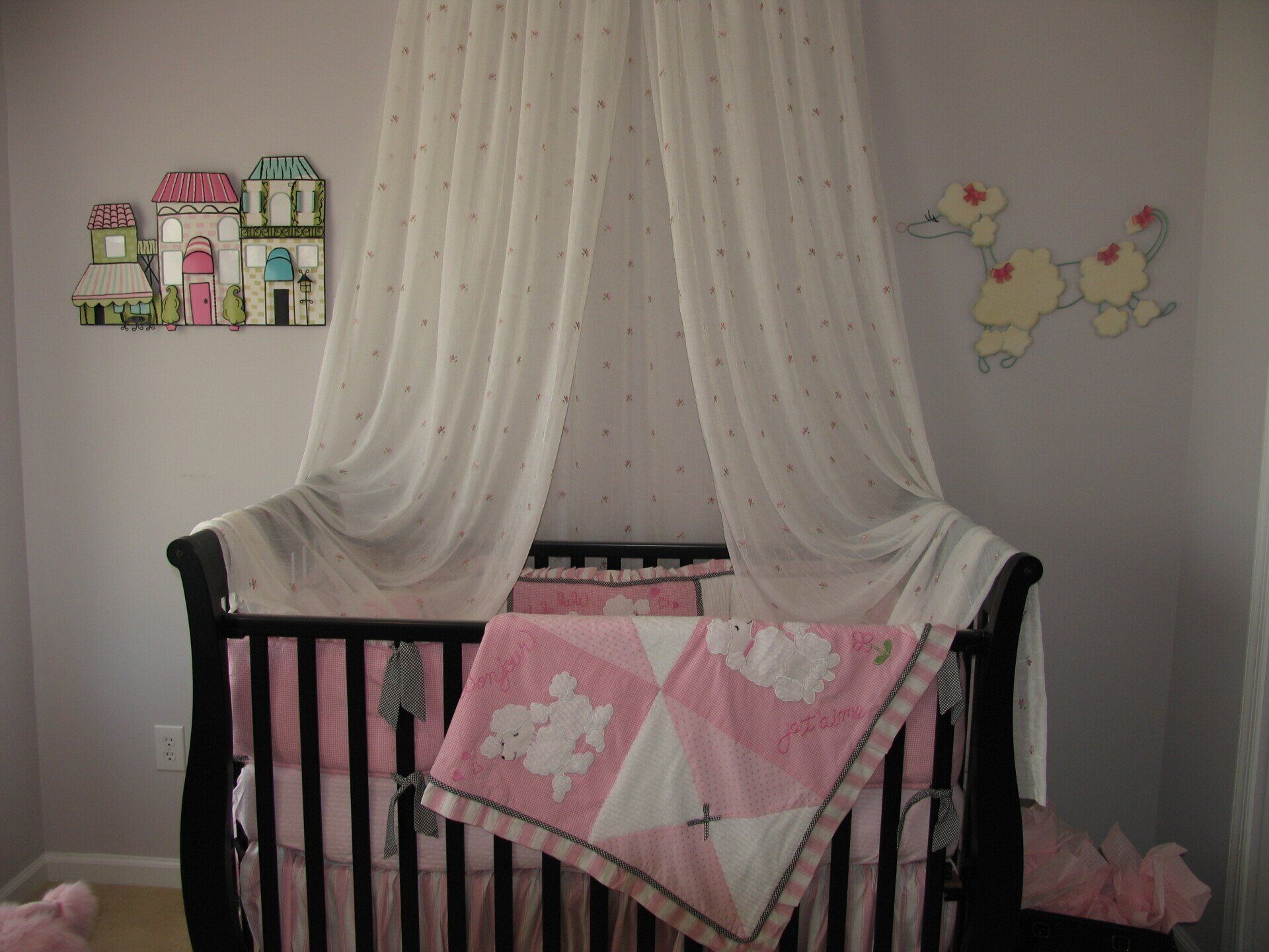 Black crib with pink bedding, white canopy, and decorative wall art in a nursery.