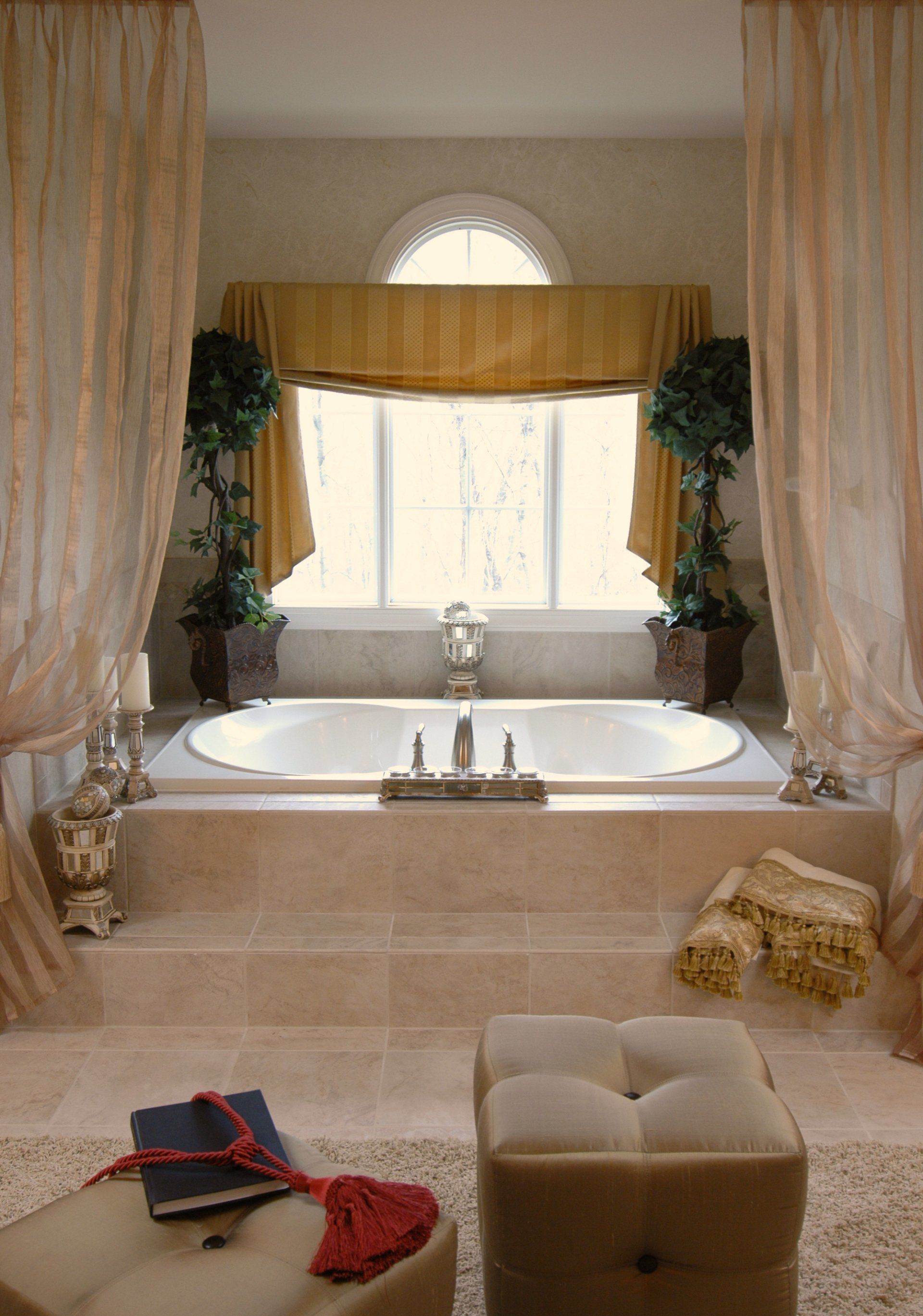 Bathroom with a large oval tub, a window, and curtains. The space is elegant and light-colored.