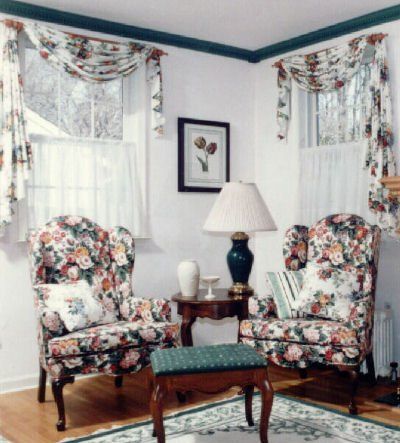 Two floral wingback chairs face each other in a corner. A small table and ottoman are between them.