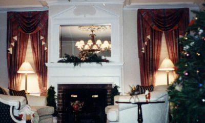 Living room with fireplace, mirror, red curtains, lamps, and Christmas tree.
