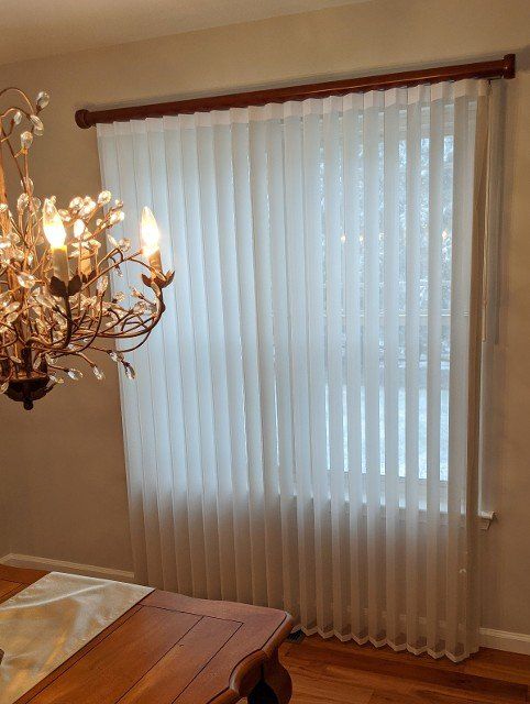 Vertical white blinds on a window, wooden trim, with a chandelier to the left.