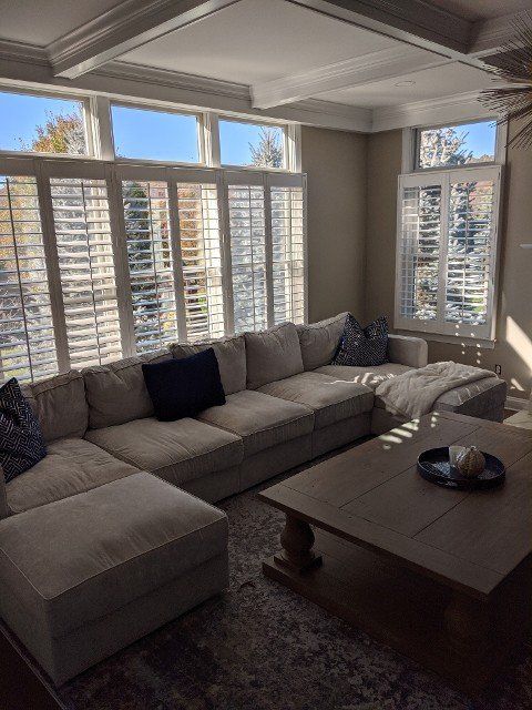 Cozy living room with a large beige sectional sofa, white shutters, and a dark wood coffee table.