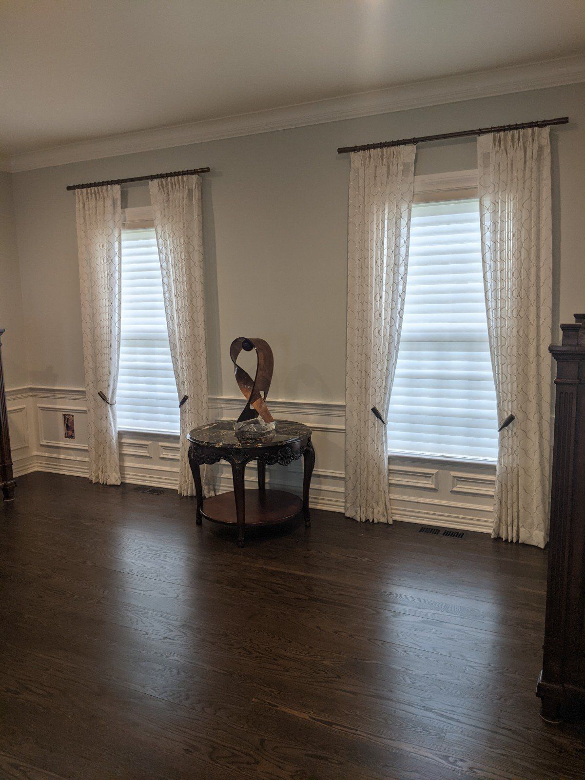 Two windows with sheer curtains, a table, and dark wood floors in a room.
